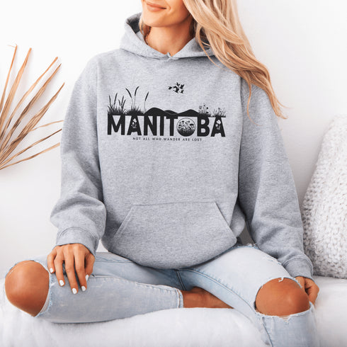 Featuring a prairie landscape, the design showcases wildflowers and prairie grasses blooming from the letters "Manitoba," artfully integrated into the scene.